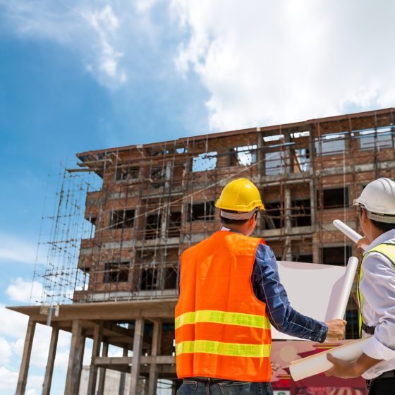 Businessman engineer looking blueprint in a building to  discussion with architects at construction site or building site of highrise building